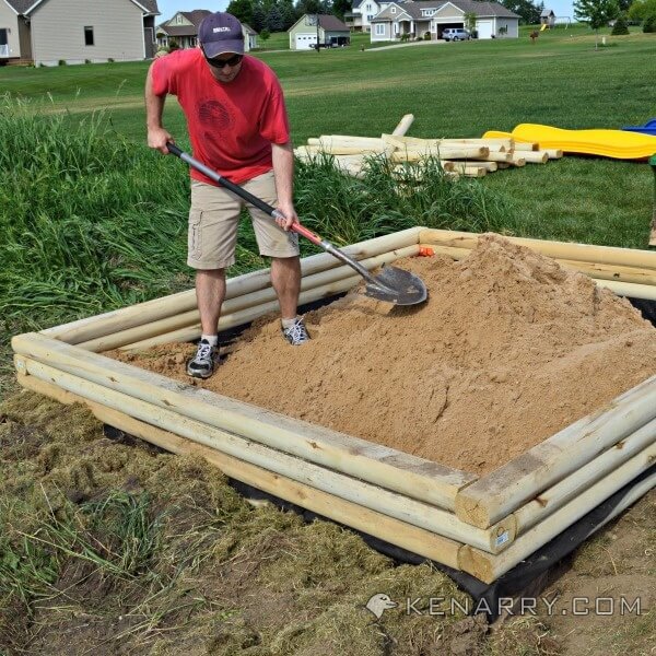 A man smoothes out sand in a new sandbox 