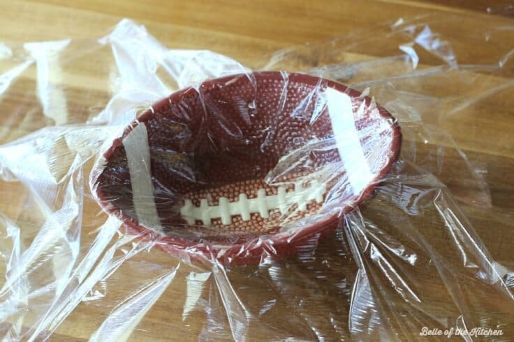 Plastic wrap covers a football-shaped bowl. 