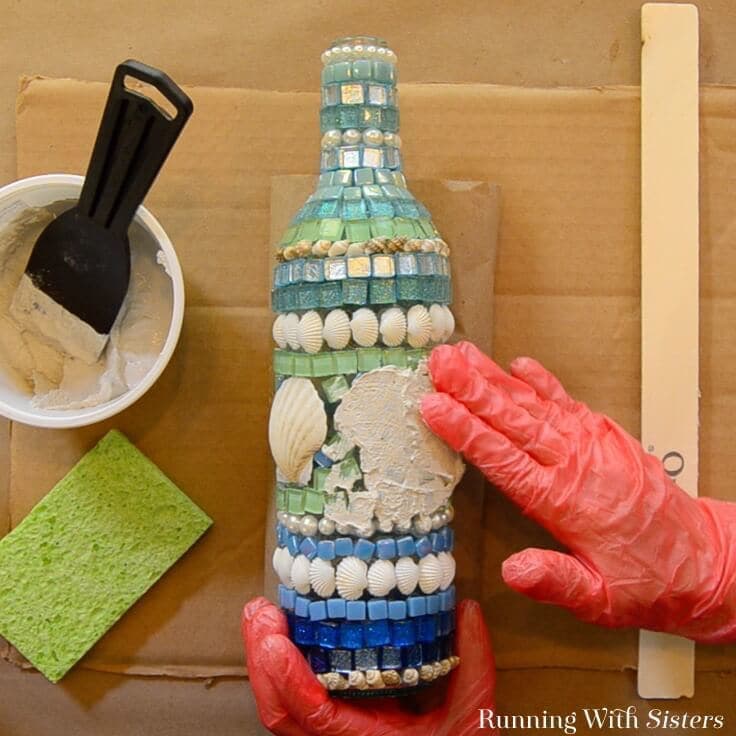 Learn how to make a mosaic wine bottle with shells and tiles! We'll show how to glue the tiles and mix the grout with a video and written steps!