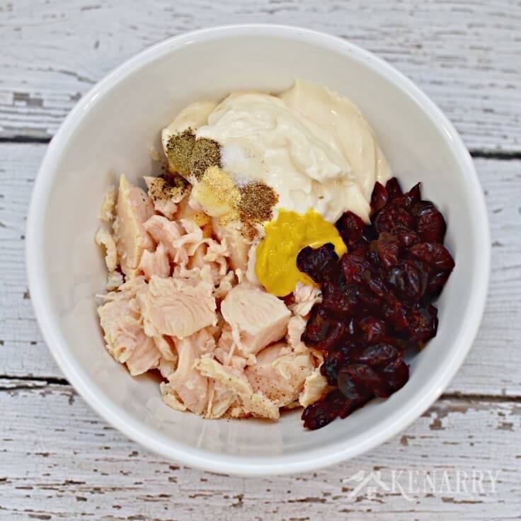 A mixing bowl with canned chicken, mayo. cranberries and mustard in it 