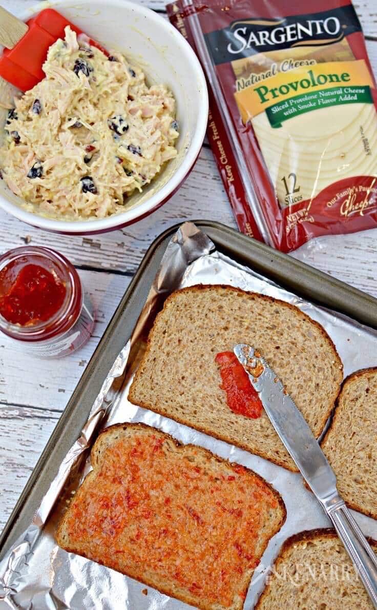 Spreading red pepper jelly on top of wheat bread