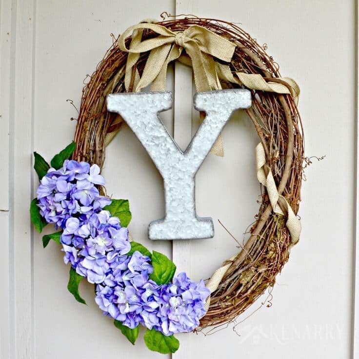 With a large industrial metal monogram and some rustic burlap ribbon this Spring Grapevine Wreath has that farmhouse style look that's so popular right now. This easy and beautiful craft idea will brighten up your front door all season long!