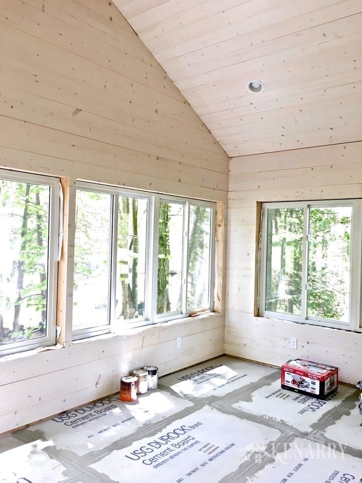 White washed pine plank walls installed in a sunroom as part of a cottage update. These shiplap walls give the room a rustic farmhouse style look. Cement board on the floor prepares the way for porcelain tile that looks like weathered wood.