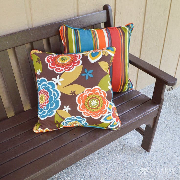 Bright colorful indoor/outdoor pillows dress up a brown polywood mission style bench on a new craftsman style front porch built on the front of an A-frame cottage home | home idea | outdoor patio | outdoor living | polywood bench