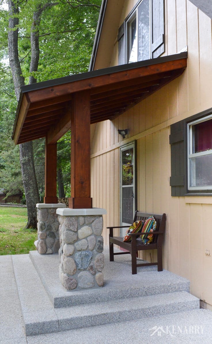 River rock pillars and cedar wood are used to create a craftsman style porch for an A-frame cottage home on a wilderness river | home idea | outdoor patio | mission style bench | exposed aggregate concrete