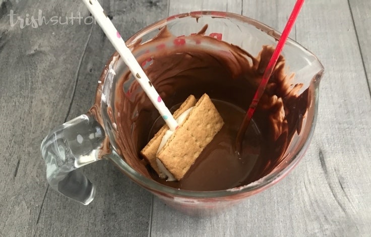 Dipping the smores on a stick into melted chocolate. 