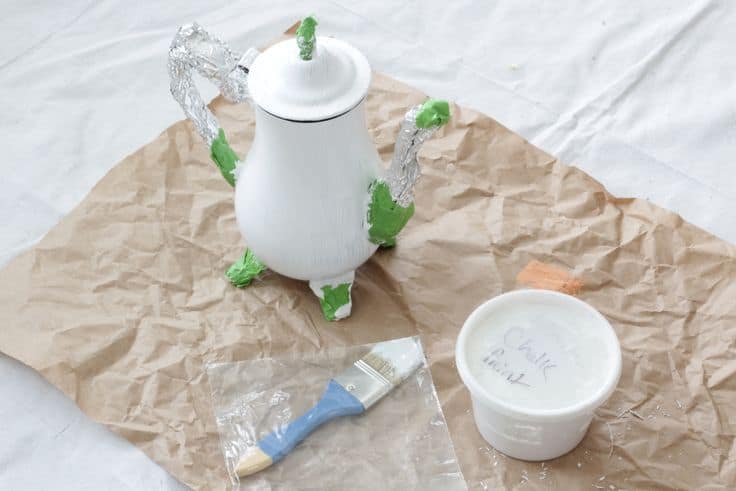 Teapot being painted with white chalk paint.