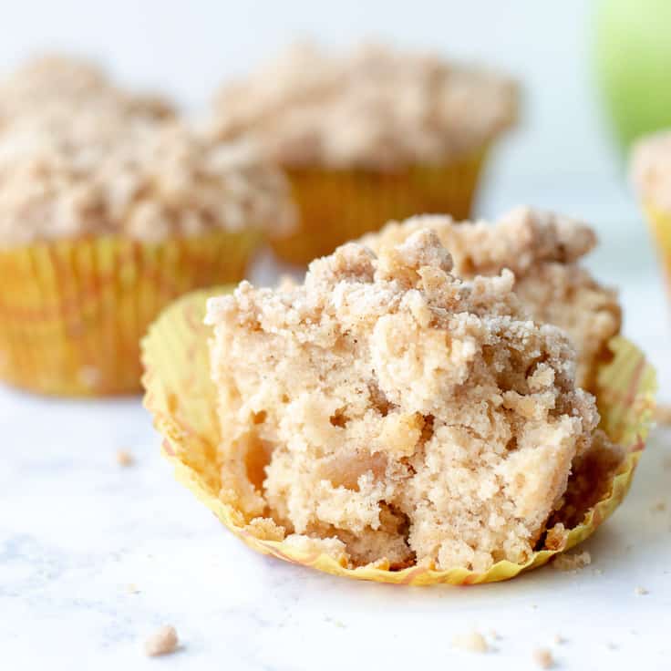 apple coffee cake muffins on a marble surface with green apples in the background