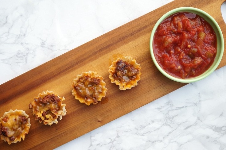 Mini Taco Cups with a bowl of salsa on a wooden cutting board