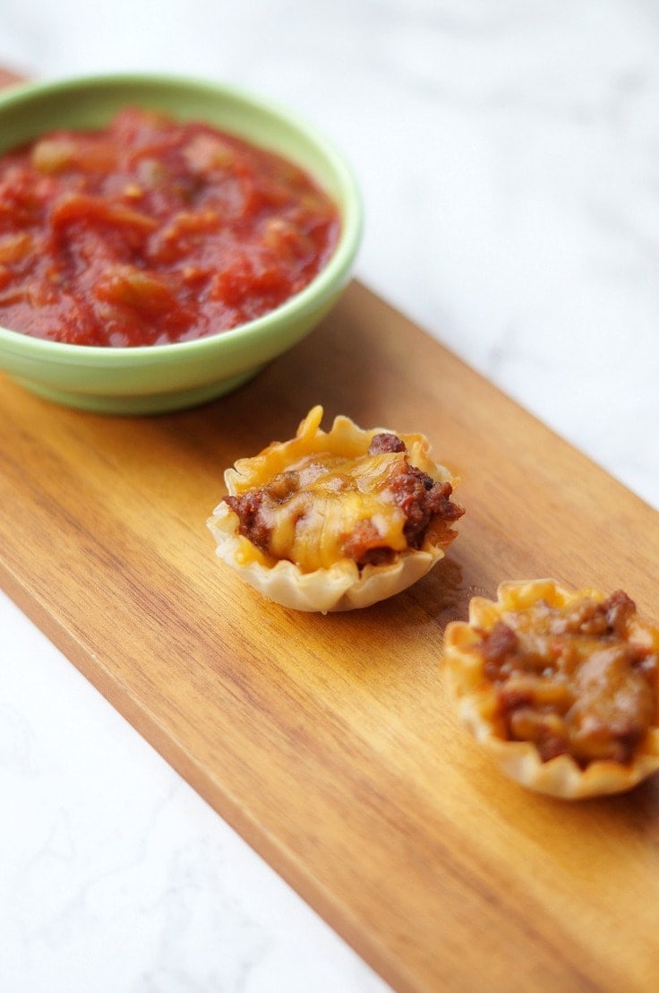 mini taco cups with a bowl of salsa on a wooden cutting board