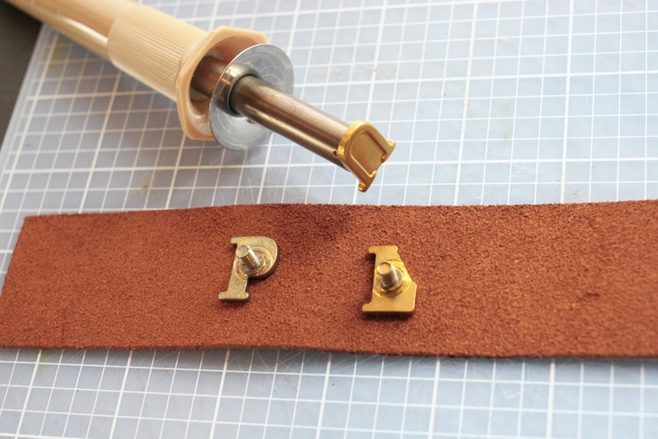 Burn the leather for a personalized leather keychain with a woodburning tool and alphabet hot stamps.