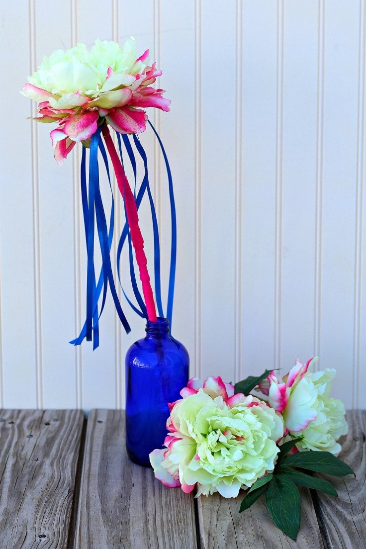 A pink flower wand with blue ribbons in a vase.