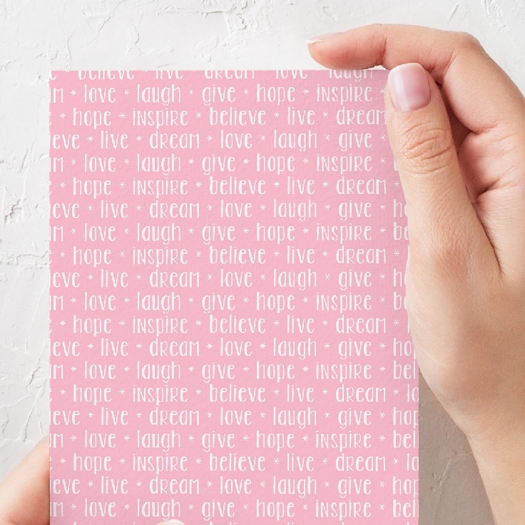 A notecard made out of pink card stock with the words love, laugh, give, hope, inspire, believe, printed on it. 