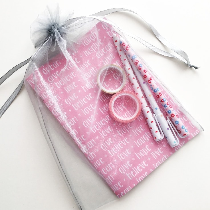 A gift bag filled with a DIY paper notebook, washi tape and pens. 