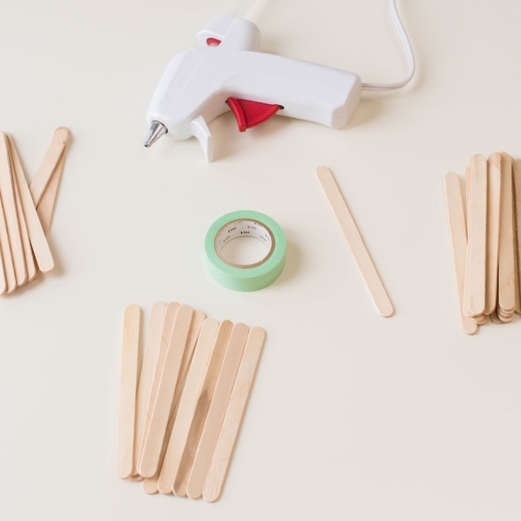 An overhead image of popsicle sticks, green washi tape and a glue gun. 