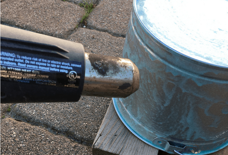 Using a heat gun to age a galvanized metal pail. 