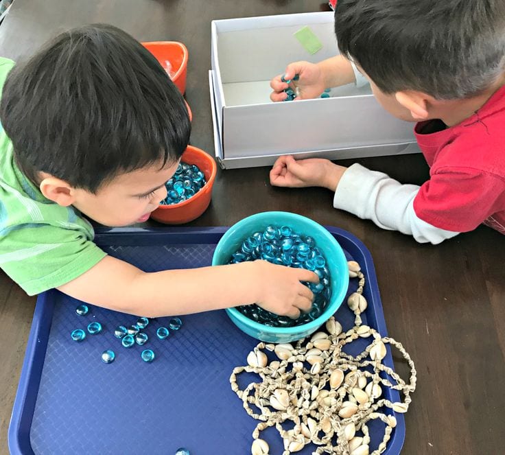 Small boys sort glass gems and seashells into different bowls. 