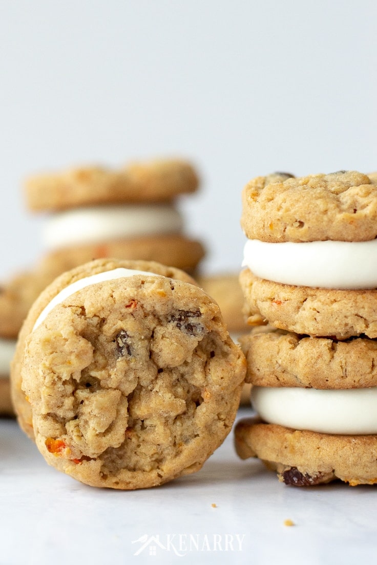An oatmeal raisin carrot cookies is standing vertically on end so you can see the chunks of minced shredded carrot. There are more carrot cake cookies stacked on top of one another in the background.