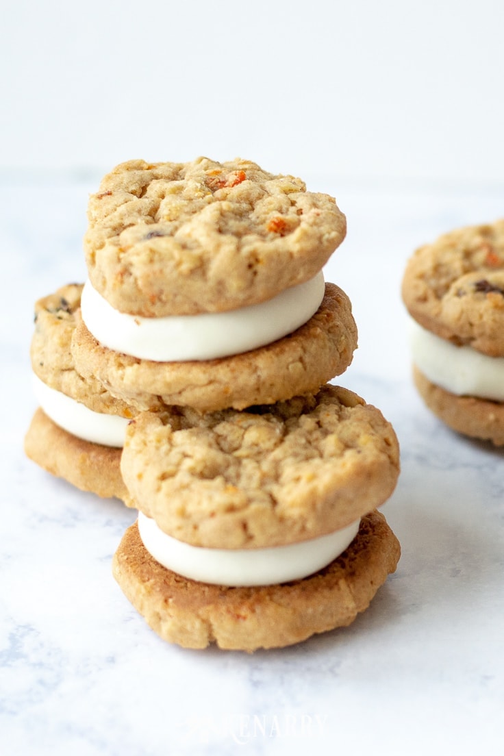 Three oatmeal raisin carrot cookies stacked in a pyramid. Cream cheese frosting in the center of each one so they taste like mini carrot cakes.