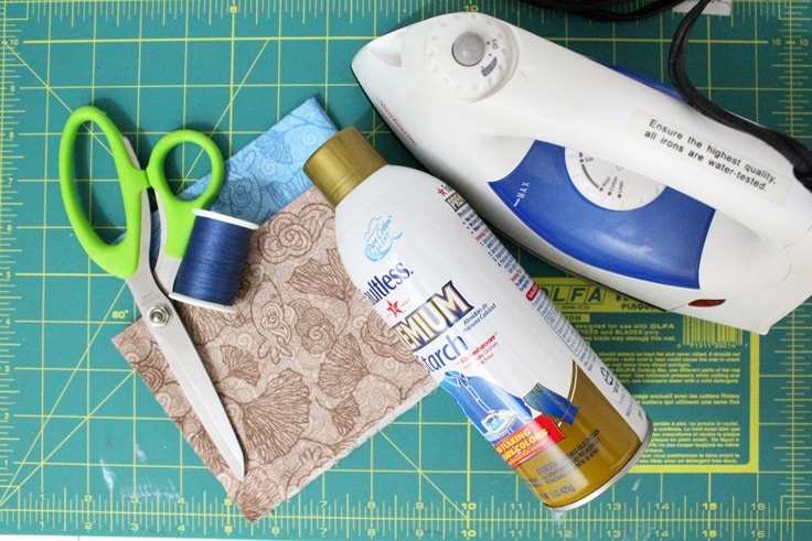 scissors, iron, fabric, thread, and starch on a craft table