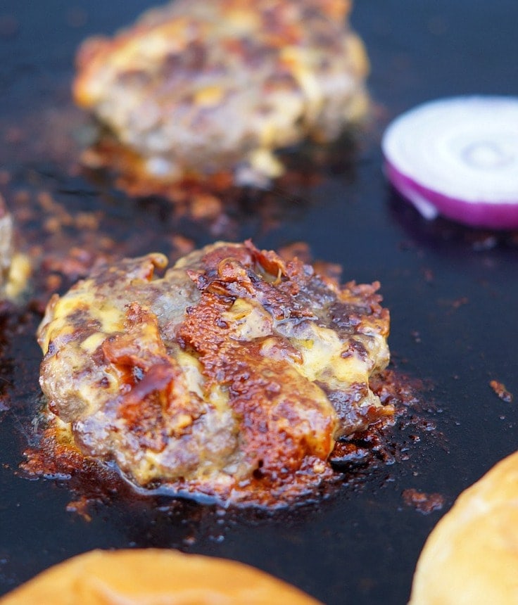 A bacon and cheddar stuffed burger cooks on the grill