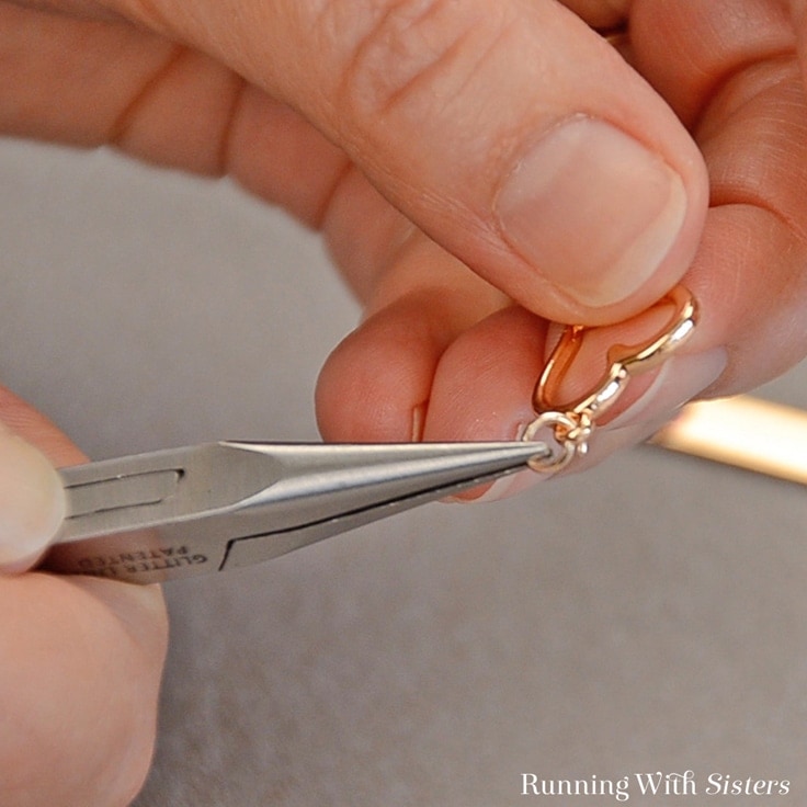 Use pliers to attach a heart charm to the DIY necklace 