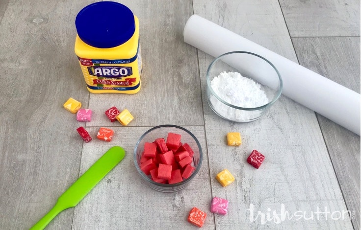 Three ingredients to create edible slime including corn starch, powdered sugar and Starburst along with a spatula and parchment paper.