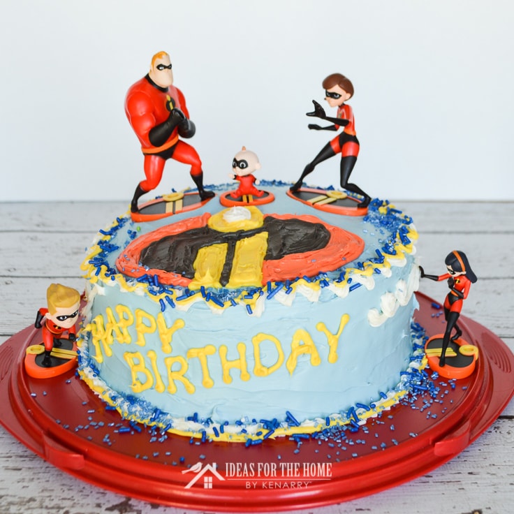 Front view of a round Incredibles birthday cake with figurines of Dash, Violet, Jack Jack, Elastigirl and Mr. Incredible