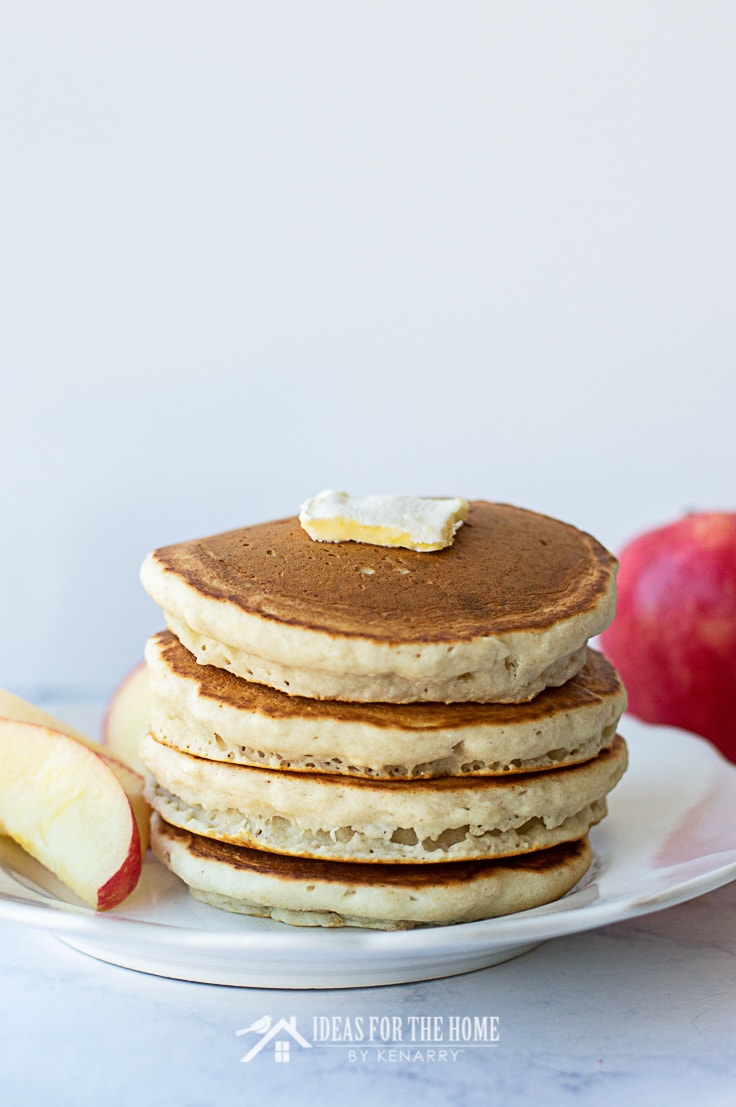 A slab of butter on top of four cinnamon pancakes along with slices of apple