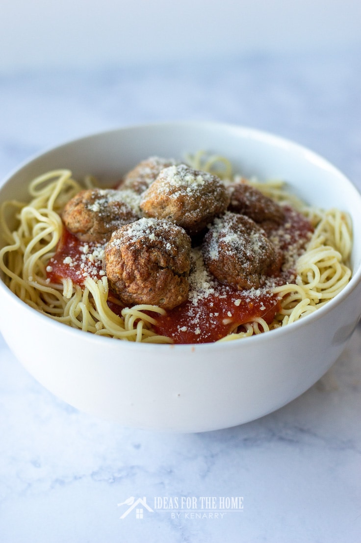 Homemade meatballs topped with parmesan cheese in a bowl full of spaghetti