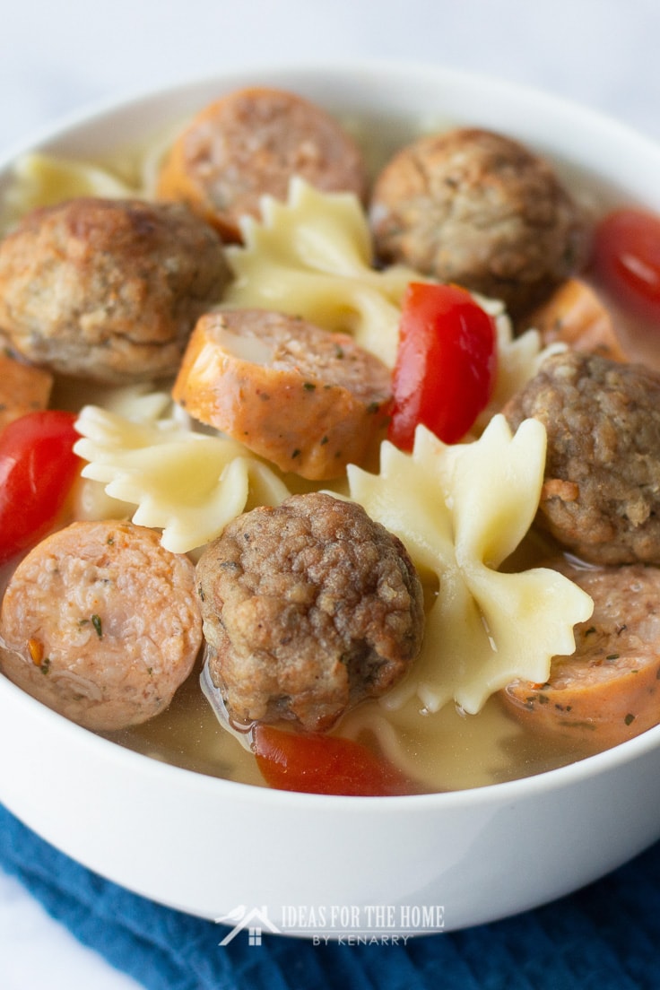 Close up of homemade meatballs, smoked turkey sausage and bow tie pasta with vegetables in a soup