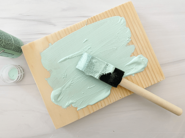 Painting a piece of wood with seafoam green paint.
