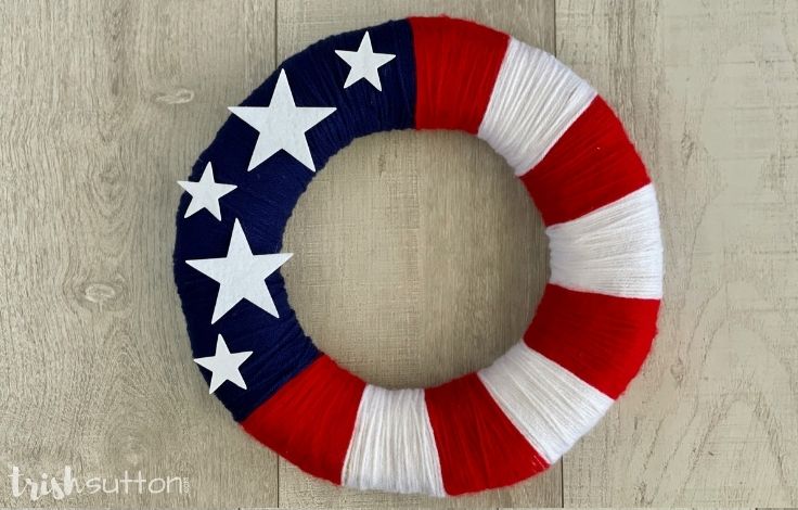 Red, white and blue DIY yarn wreath on a wood background.