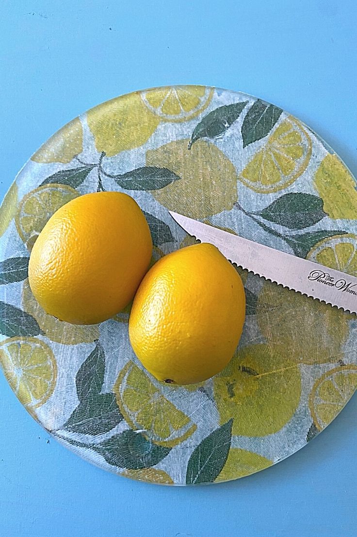 Two whole lemons on a glass cutting board with a knife.
