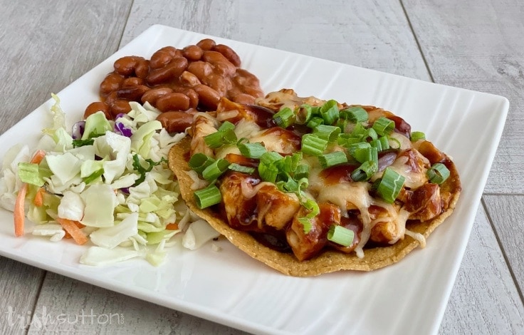 BBQ Chicken Tostada plated with chopped salad & chili beans on a white plate.